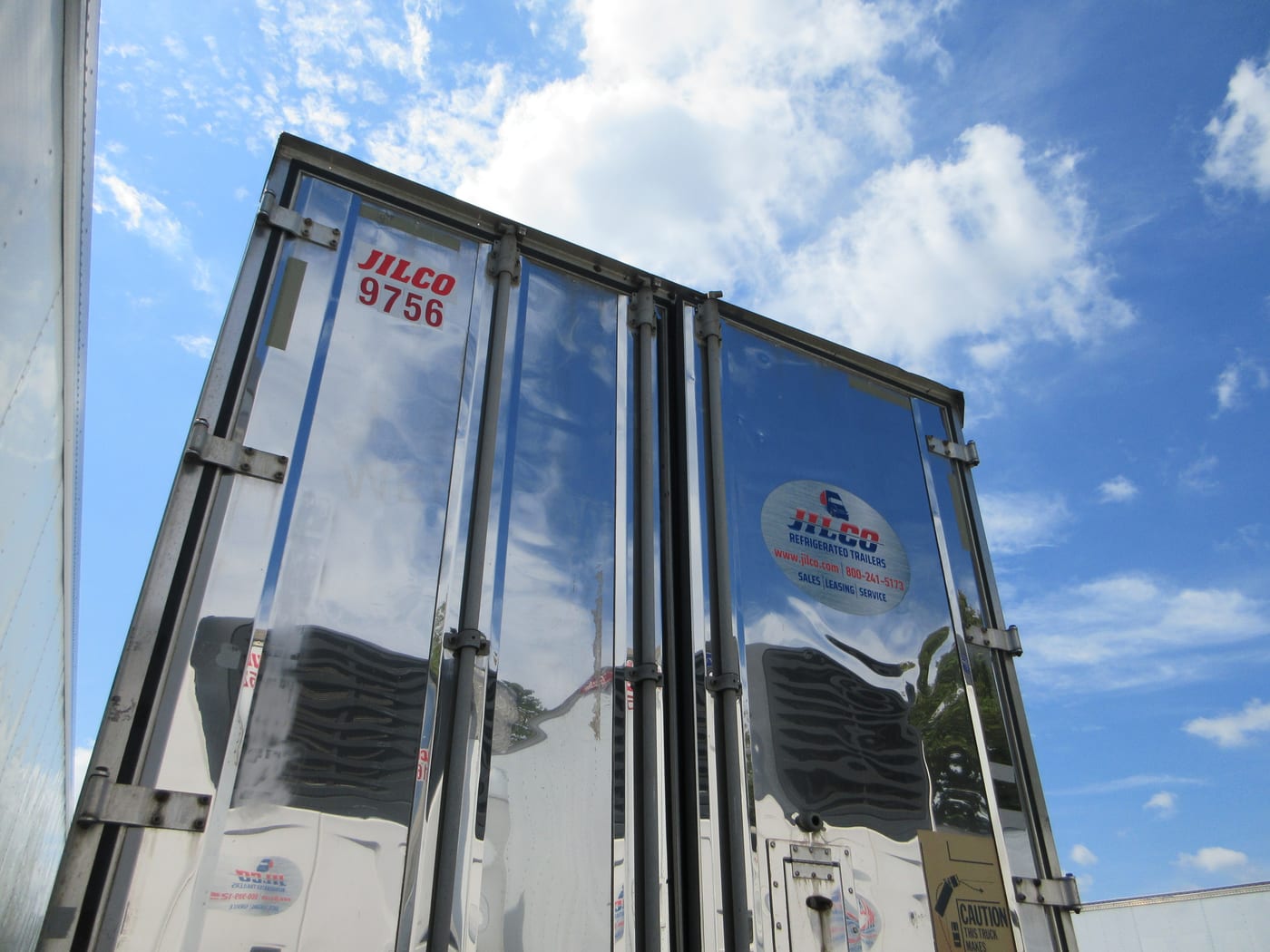 The rear doors of a Jilco refrigerated trailer seen from below against an open sky, the kind of unit parked on site for an event.